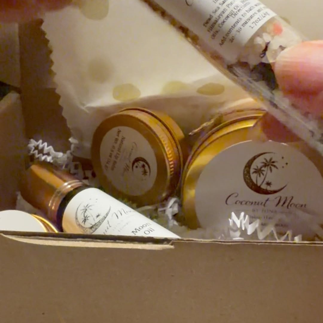 A Coconut Moon Signature Box: gold-lidded candle and bath-salt jars, a perfume oil, and the Coconut Moon logo card nestled in a kraft gift box.