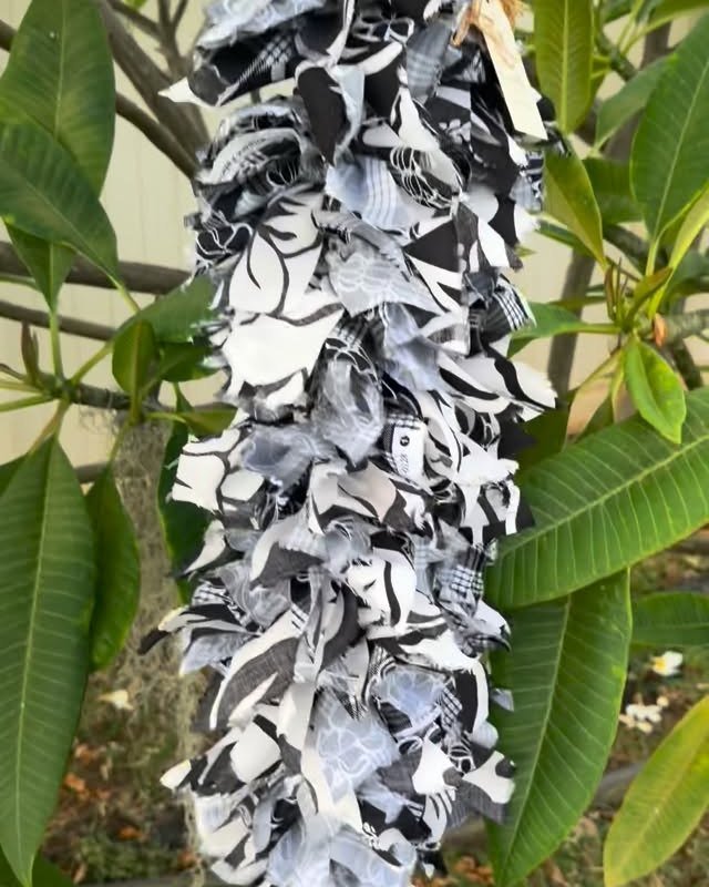 A handmade black-and-white fabric Cook Island Maile-style lei hanging among plumeria leaves.